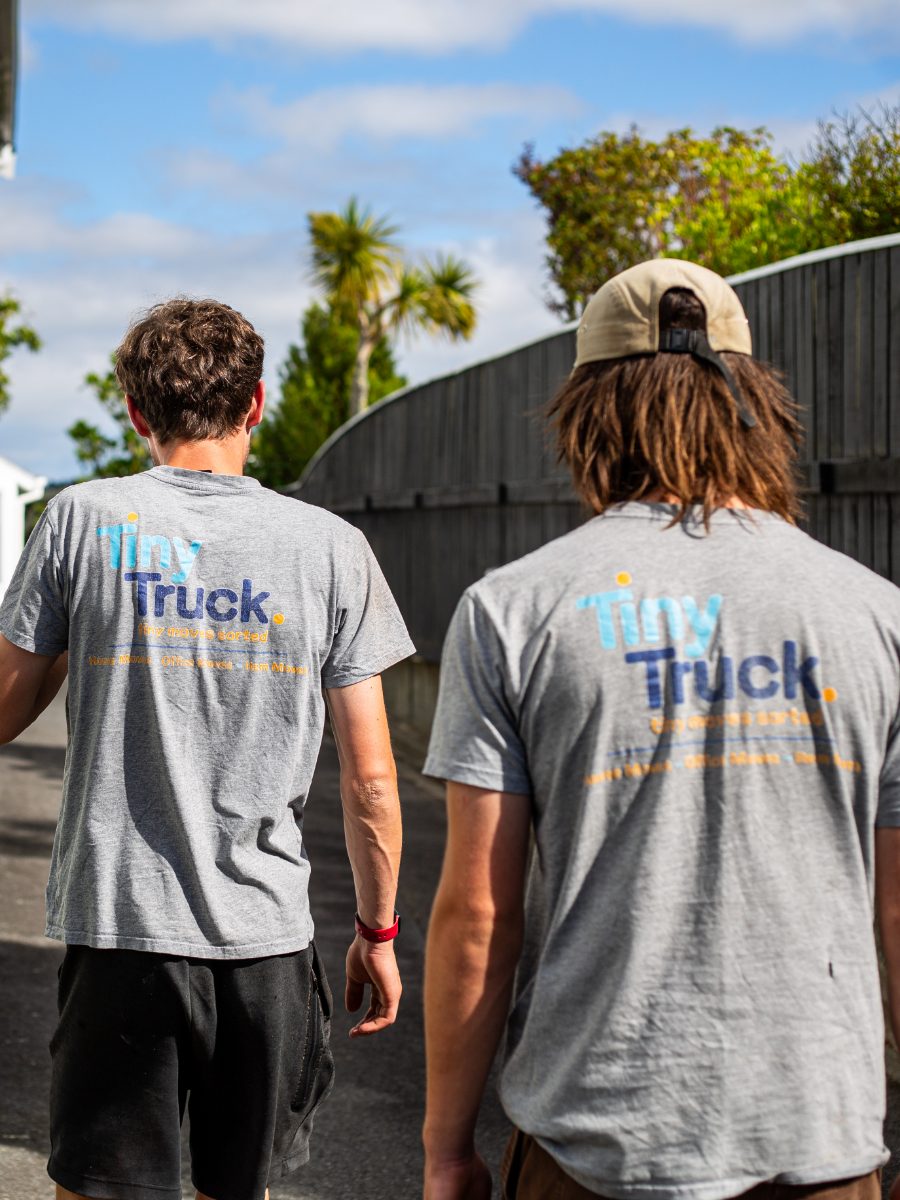 Two crew members in grey Tiny Truck tee shirts walking up a sunny driveway